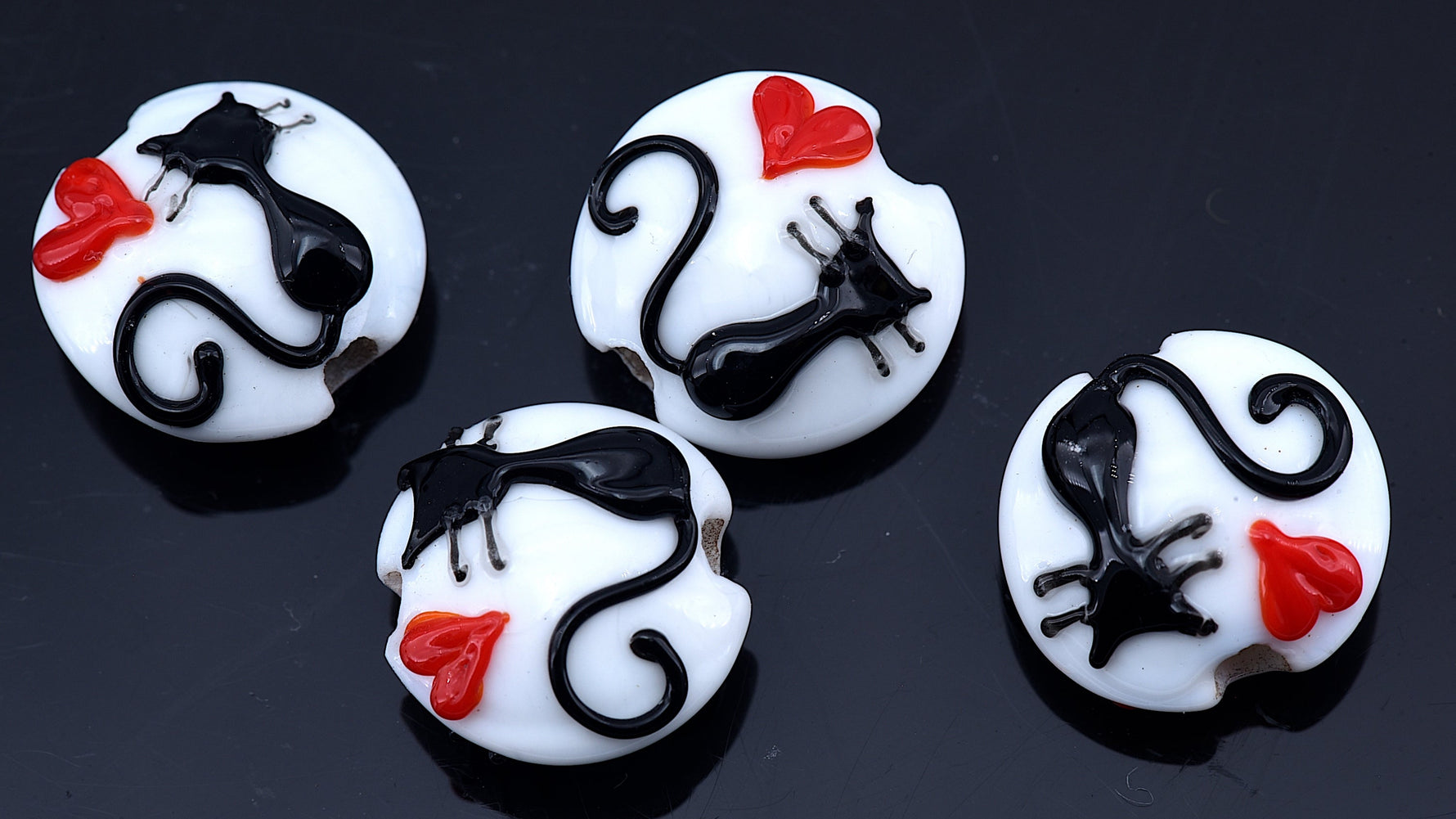 Four white buttons with black cat designs and red bows on a dark background