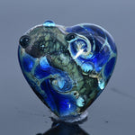 Heart-shaped blue glass bead on a reflective surface with a gray background