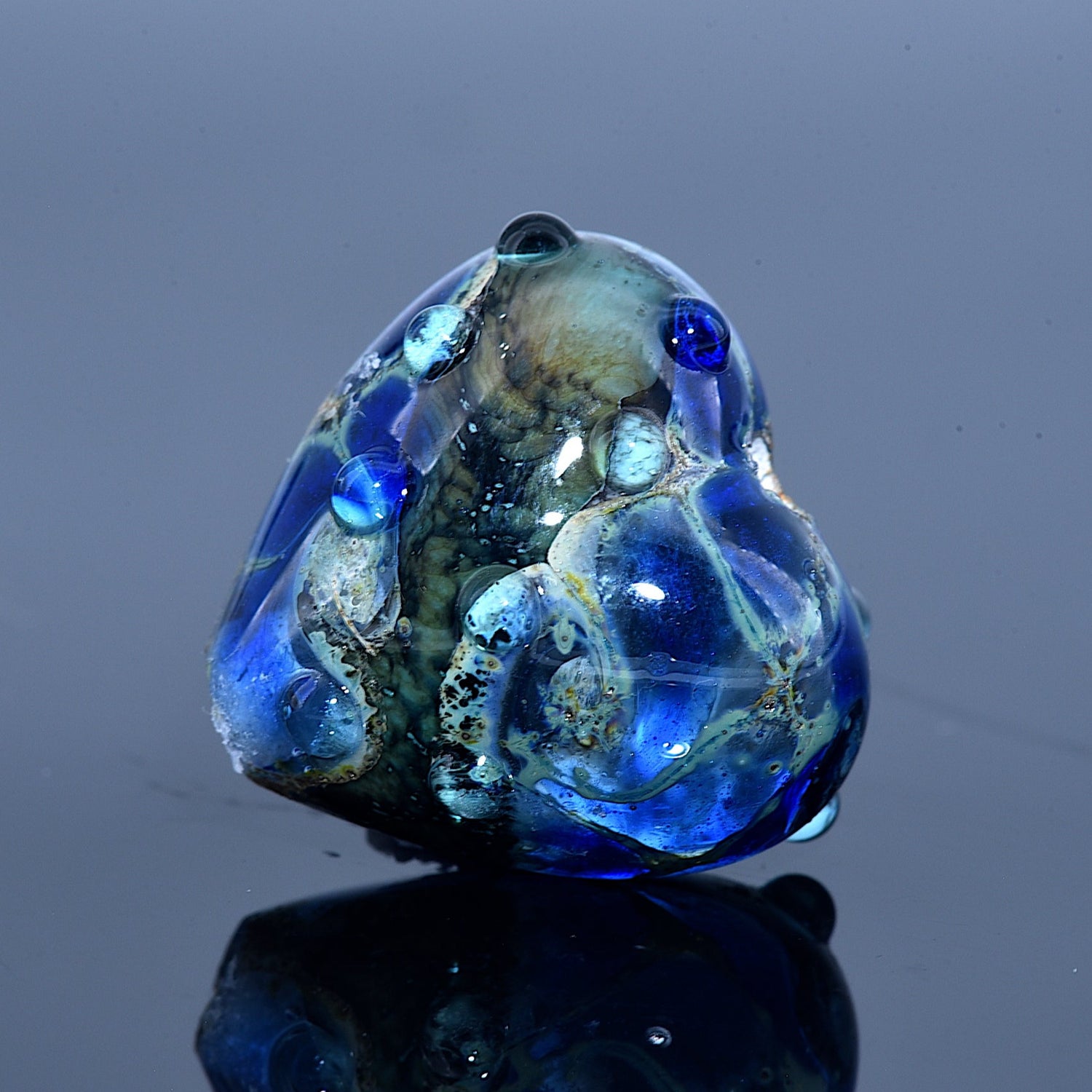 Glass frog sculpture with blue and green colors on a reflective surface
