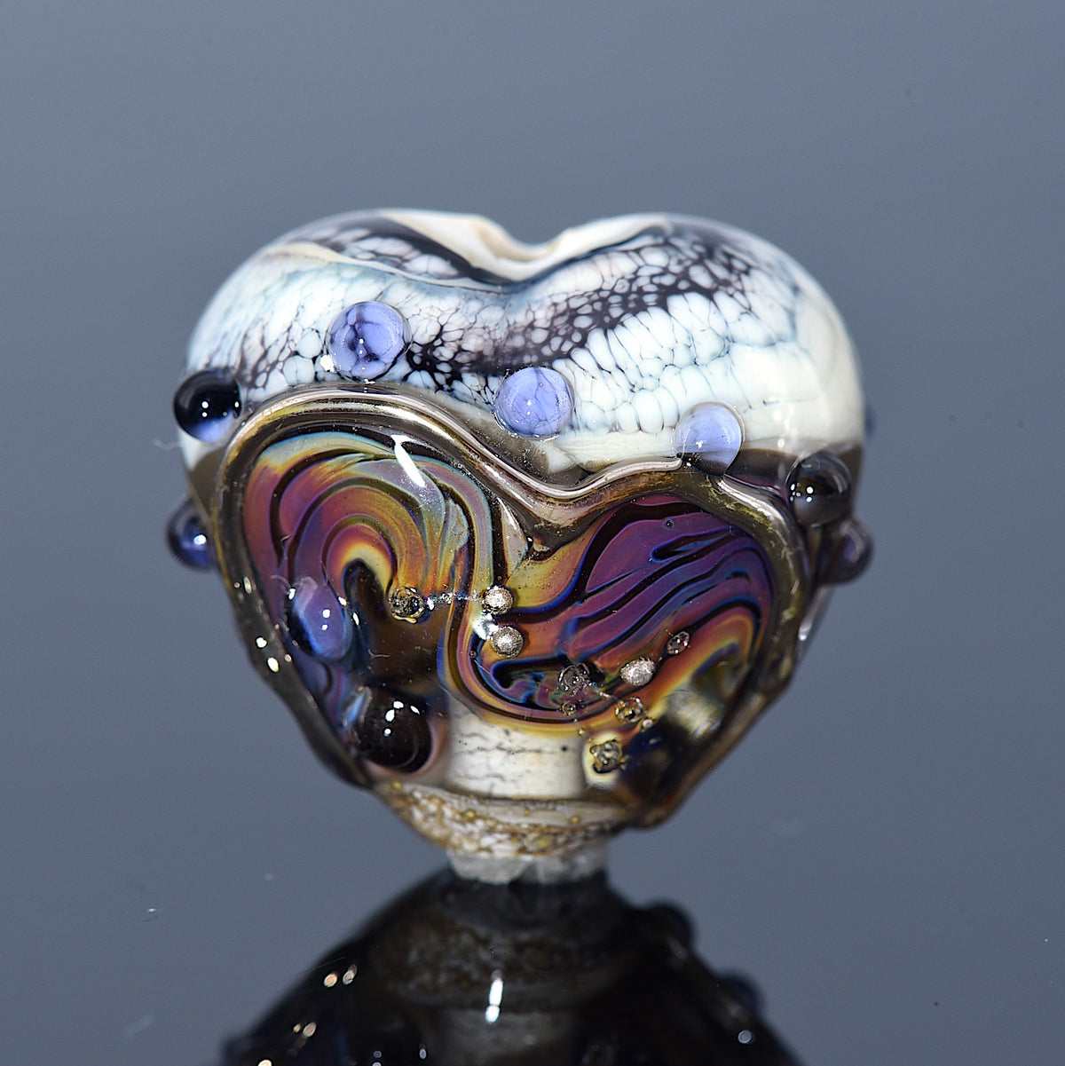 Heart-shaped glass bead with multicolored design and embedded stones on a dark background