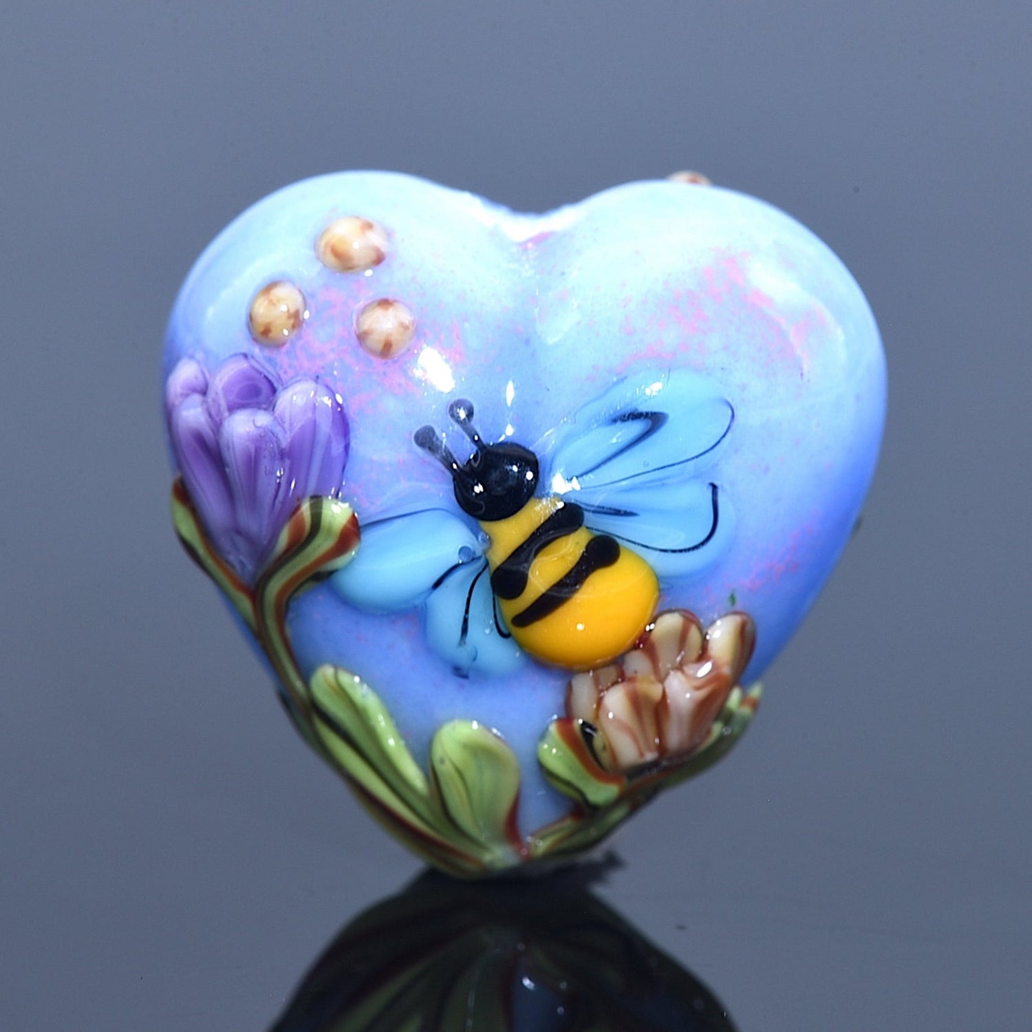 Heart-shaped object with a bee and flower design on a reflective surface