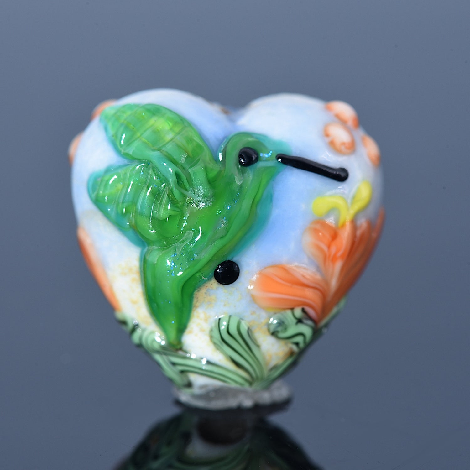 Heart-shaped object with a green bird design on a gray background