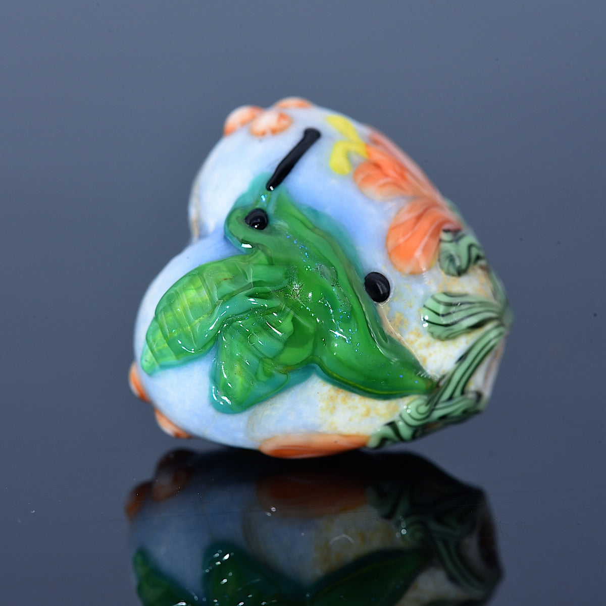 Decorative glass bead with green leaf design on a reflective surface