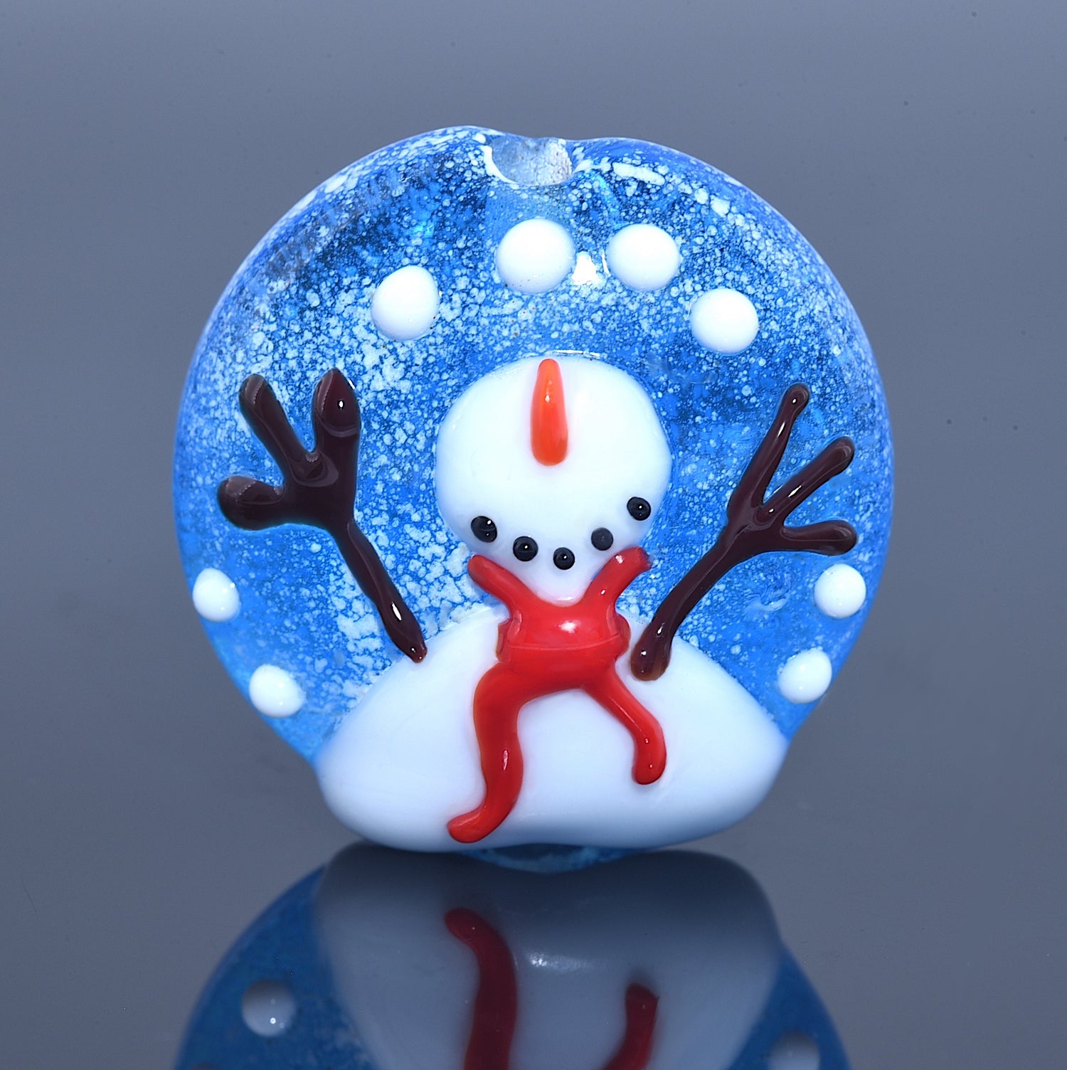 Glass snow globe with a small snowman figure inside on a reflective surface.