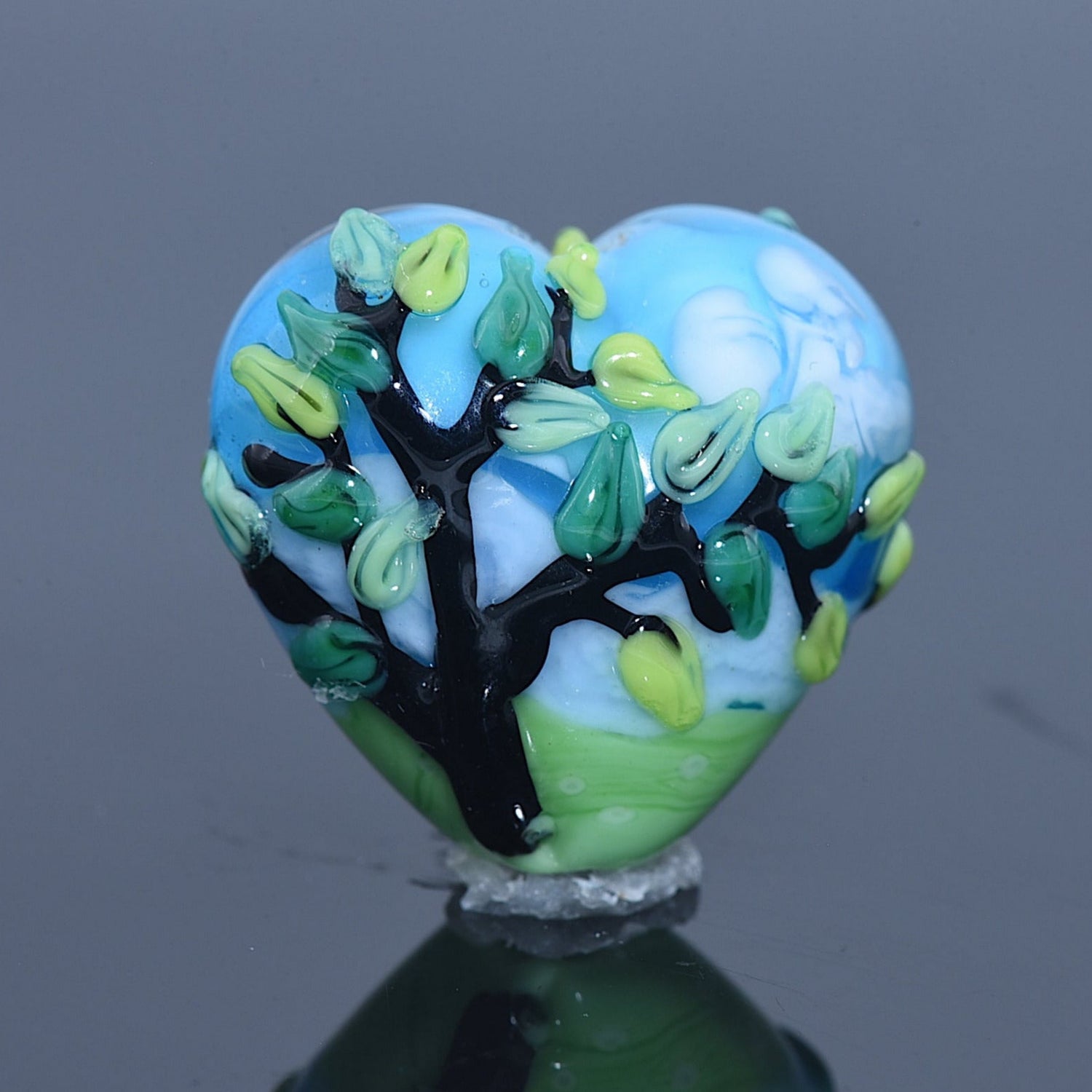 Heart-shaped glass ornament with tree design on a reflective surface
