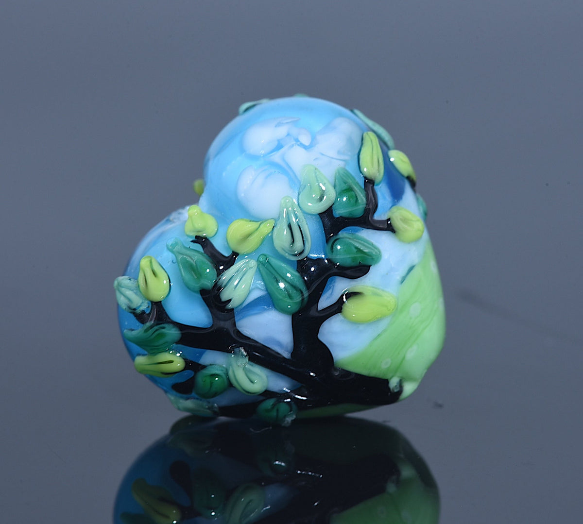 Glass bead with tree design on a reflective surface