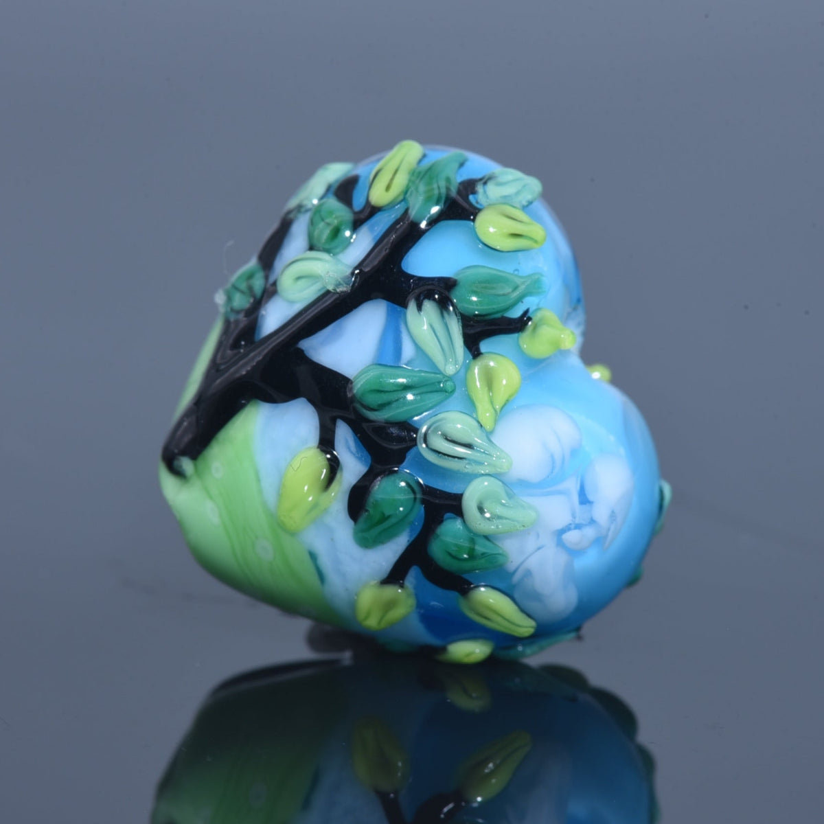 Decorative glass bead with tree design on a reflective surface