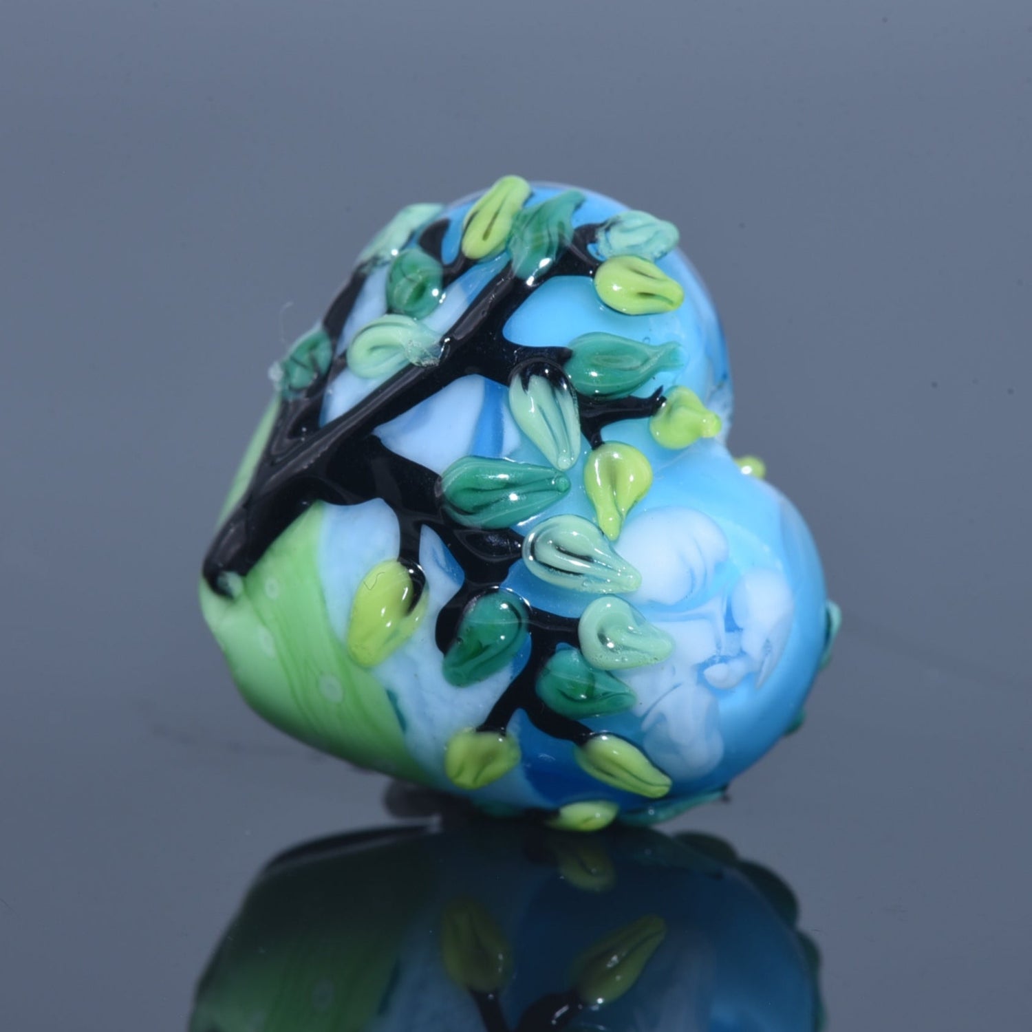Decorative glass bead with tree design on a reflective surface