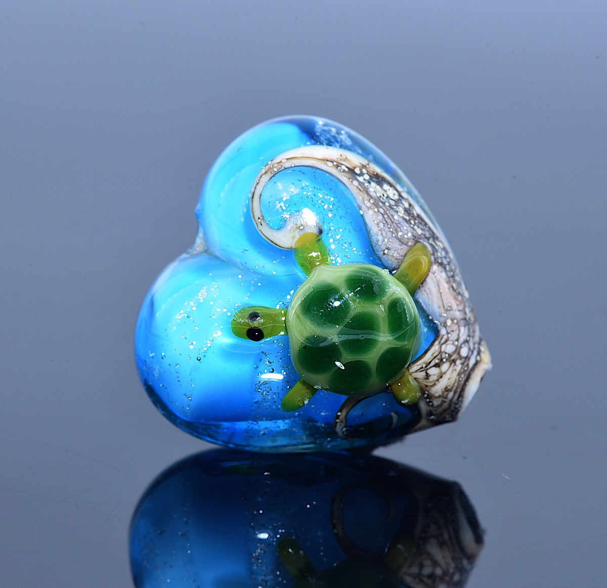 Glass heart with a green turtle design on a reflective surface