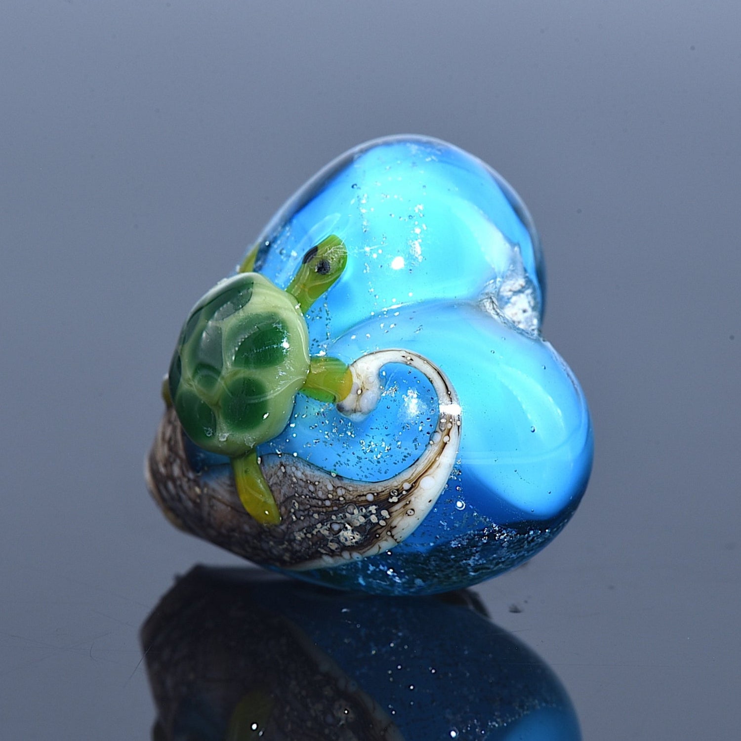 Blue heart-shaped object with a green turtle design on a reflective surface