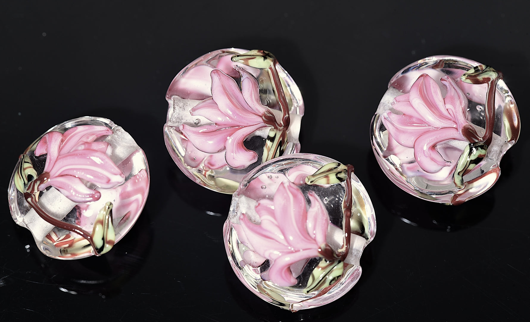 Four pink floral glass beads on a black background