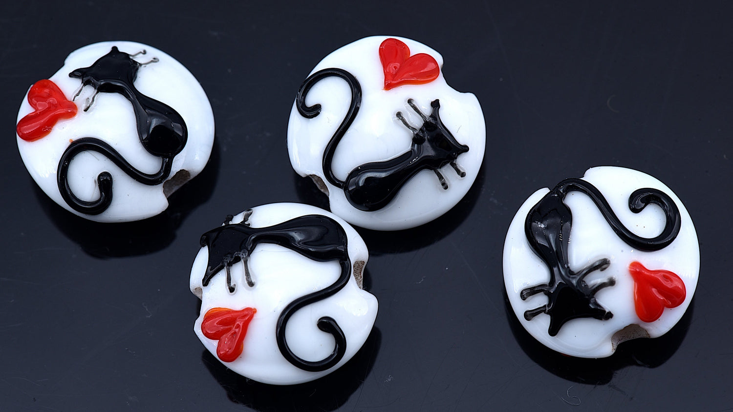 Four white buttons with black cat designs and red bows on a dark background
