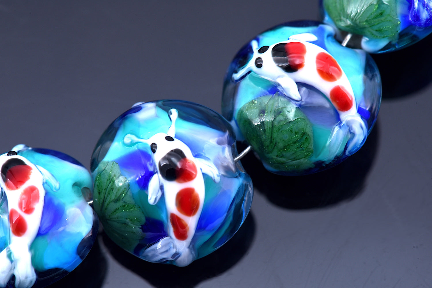 Glass beads with fish and lotus designs on a dark background