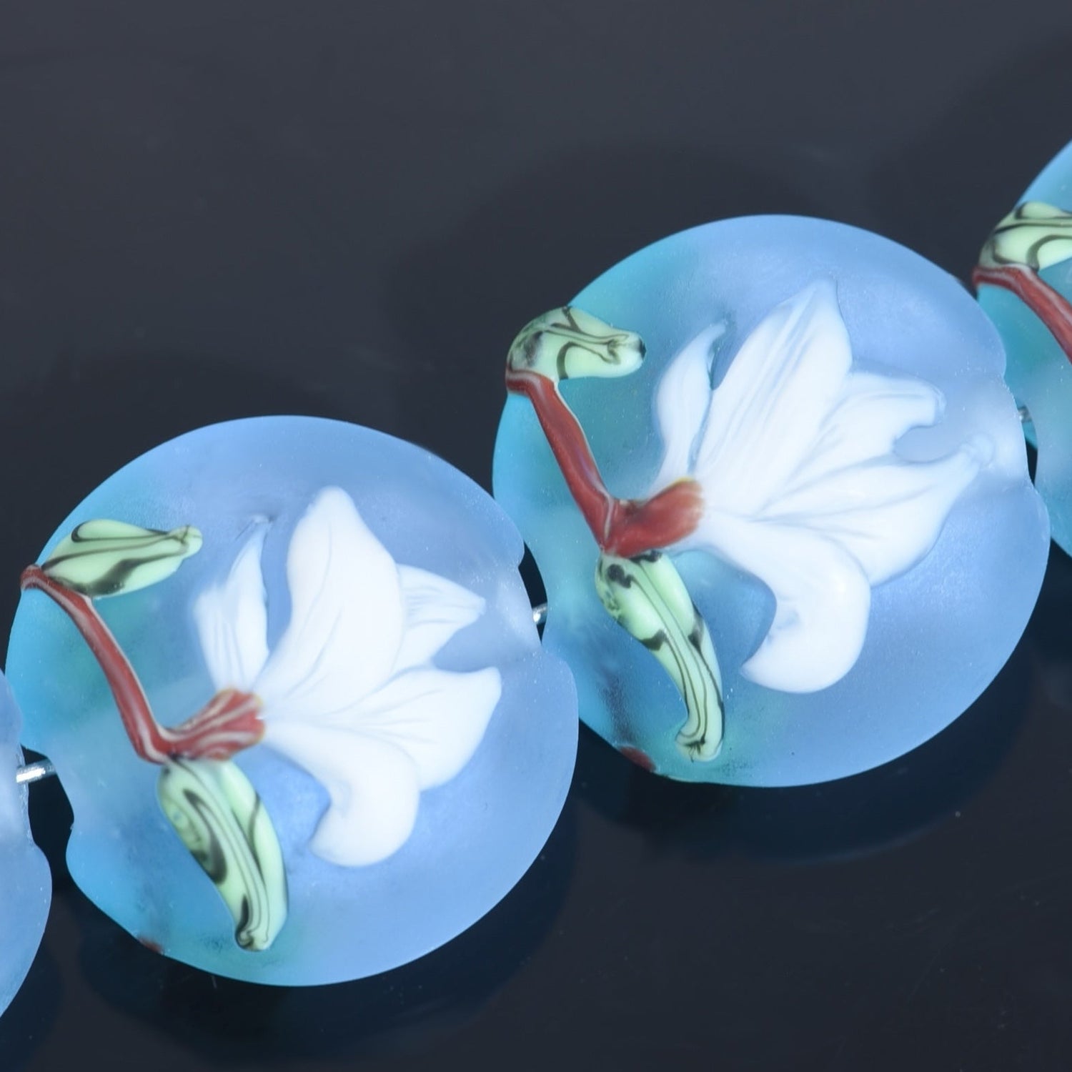 Blue glass beads with floral designs on a dark background