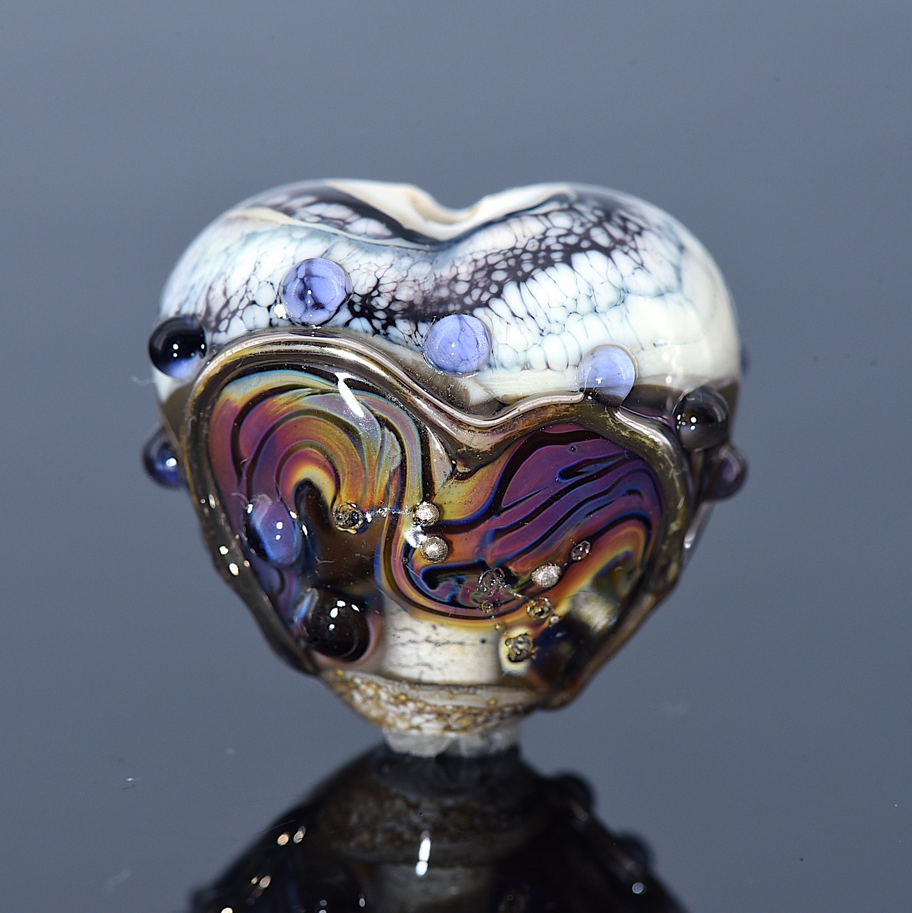 Heart-shaped glass bead with multicolored design and embedded stones on a dark background