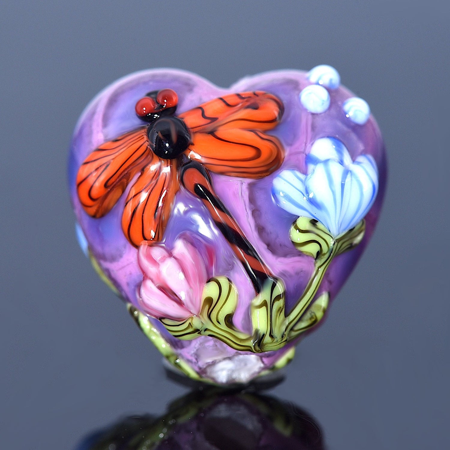 Heart-shaped glass ornament with a butterfly and flowers on a reflective surface