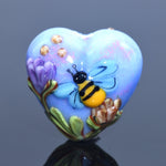 Heart-shaped object with a bee and flower design on a reflective surface