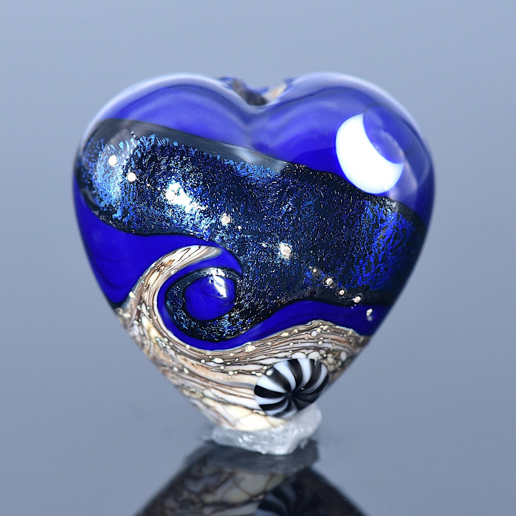 Heart-shaped glass sculpture with blue and silver design on a reflective surface