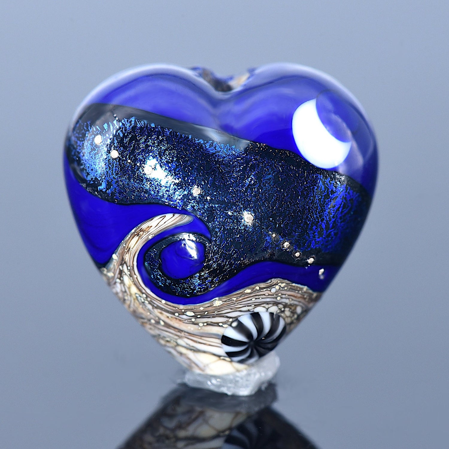 Heart-shaped glass sculpture with blue and silver design on a reflective surface