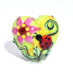 Colorful heart-shaped object with floral design and ladybug on a white background