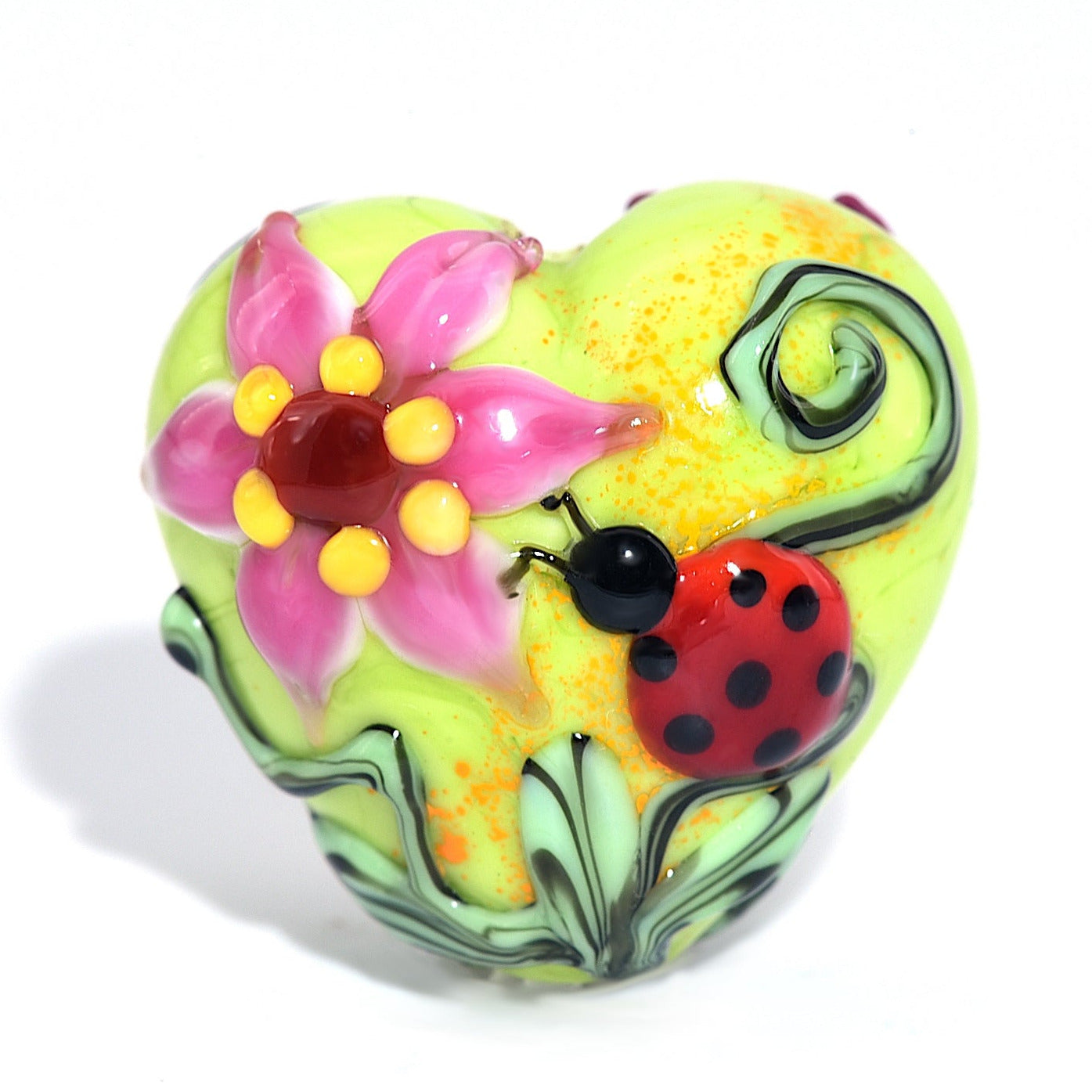 Colorful heart-shaped glass bead with floral design and ladybug on a white background