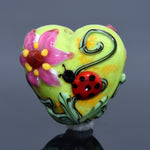 Colorful heart-shaped object with floral design and ladybug on a reflective surface