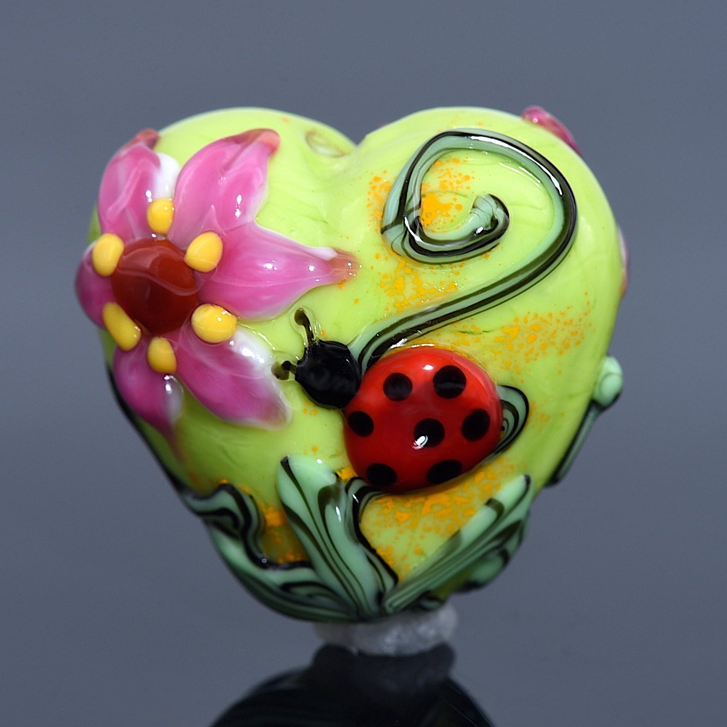 Colorful heart-shaped object with floral design and ladybug on a gray background