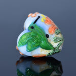 Decorative glass bead with green leaf design on a reflective surface