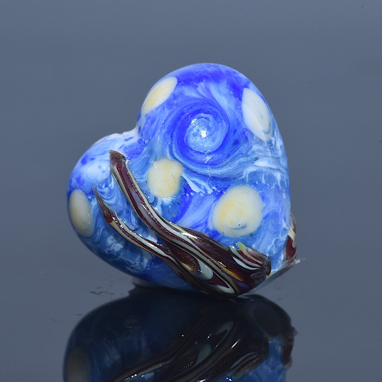 Blue glass heart bead with white and brown accents on a reflective surface