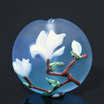 Decorative glass piece with white flowers and a red branch on a dark background
