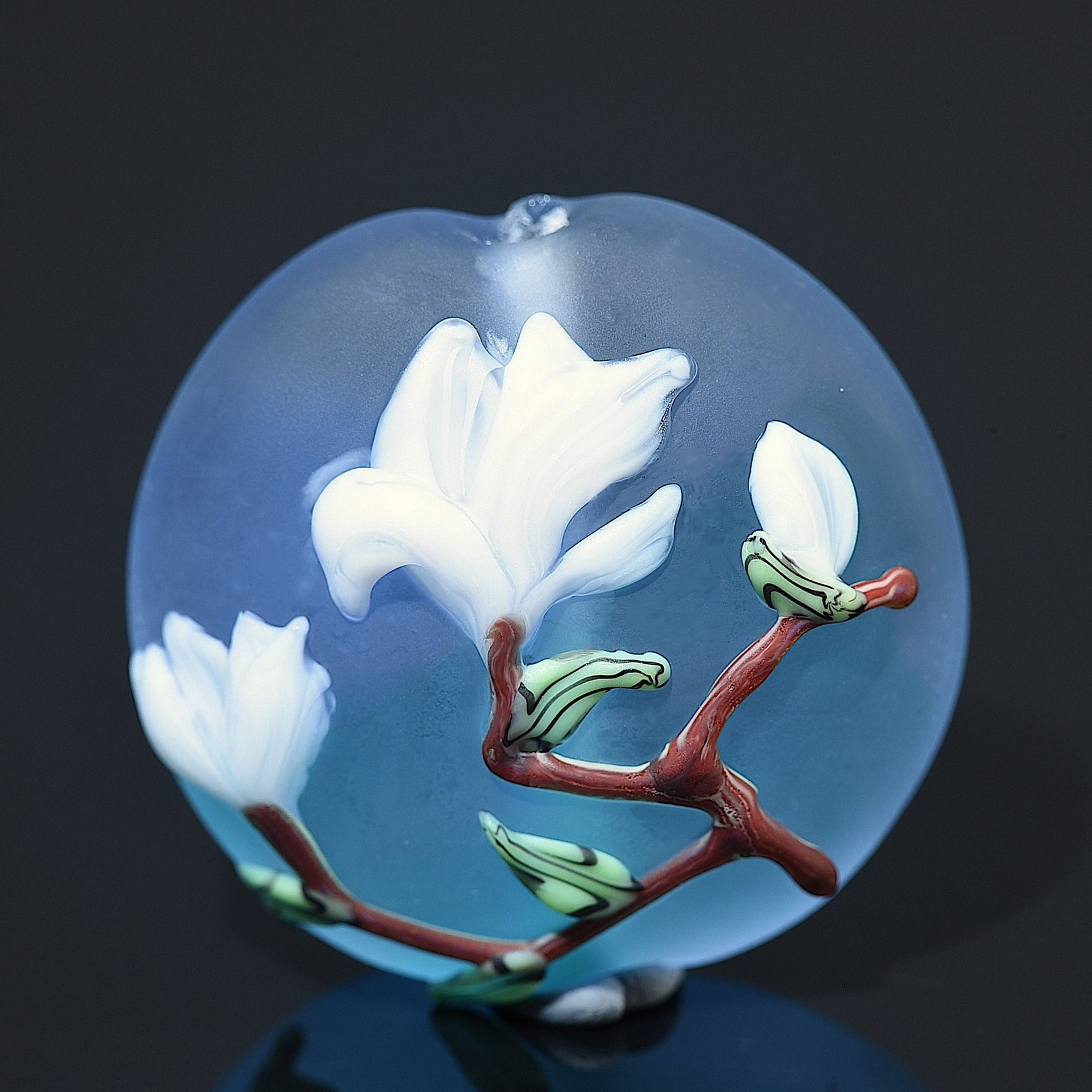 Decorative glass piece with white flowers and a red branch on a dark background