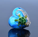 Glass heart with a green turtle design on a reflective surface
